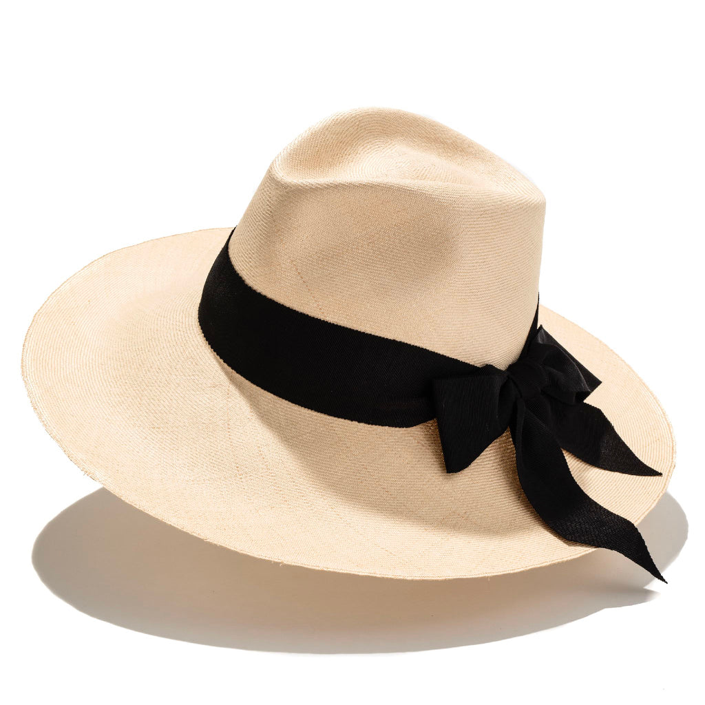 A beige wide-brimmed hat with a black ribbon around the crown, made from handwoven buntal straw with cotton grosgrain trim.